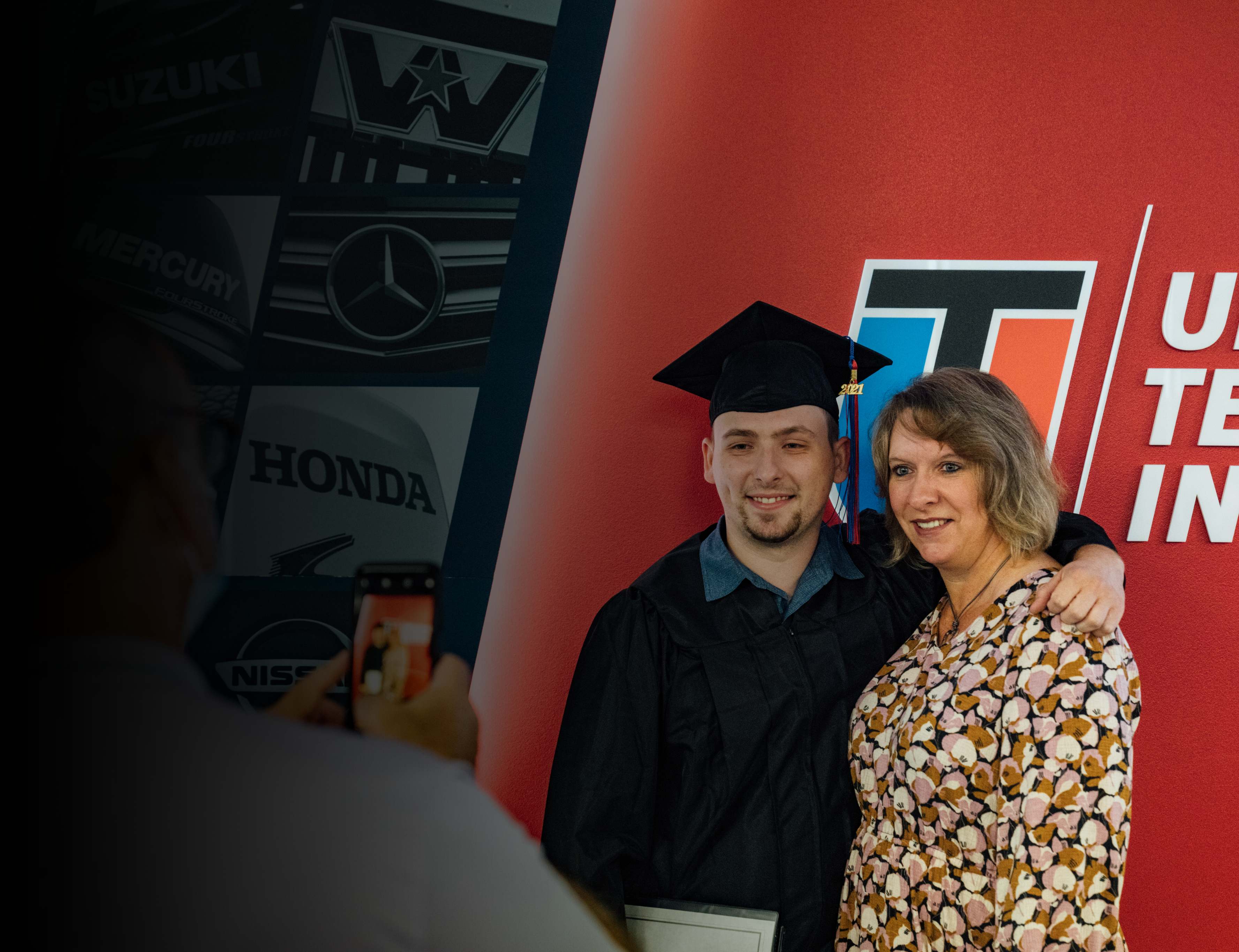 UTI trade school graduate wearing a black cap and gown with honor cords, smiling at commencement ceremony.