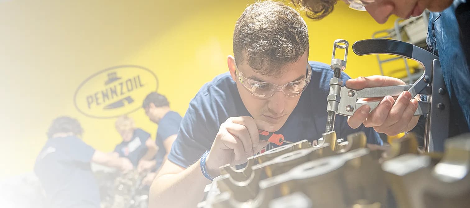 UTI trade school graduate wearing a black cap and gown with honor cords, smiling at commencement ceremony.