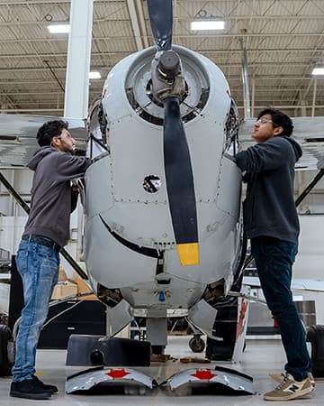 Students work together on an aircraft engine in a lab, inspecting and making adjustments.