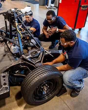 Trade school students work under the hood of a car during hands-on automotive training.