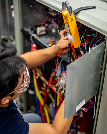 UTI instructor guides a student through wiring an HVACR system in a trade school lab.