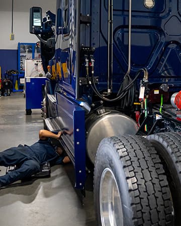 Trade school students work under the hood of a car during hands-on automotive training.